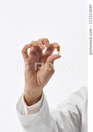 Close up photo of young woman, nurse in uniform holding one capsule, medical pill against white studio background. 121323695