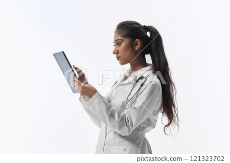 Side view young attractive Indian woman working in tablet, conducts receptions, provides online consultations against white studio background. Side view young attractive Indian woman working in tablet, conducts receptions, provides online consultations against white studio background. 121323702
