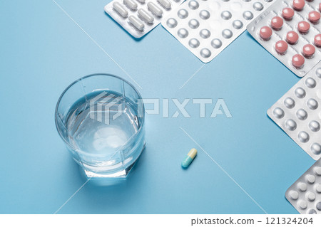Glass of water and blister packs with capsules and pills. Glass of water and blister packs with capsules and pills. 121324204