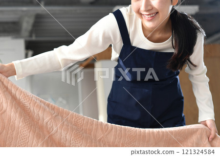 A woman in an apron making a bed 121324584