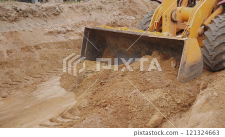 A construction vehicle digging and moving soil on a building site, showcasing heavy machinery in action. 121324663
