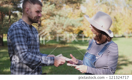 A man and a woman are engaged in a friendly cash transaction in a vibrant outdoor setting surrounded by nature 121324717