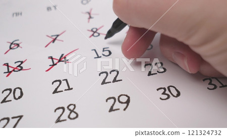 A hand skillfully using a pen to mark significant and important dates on a printed calendar for planning 121324732