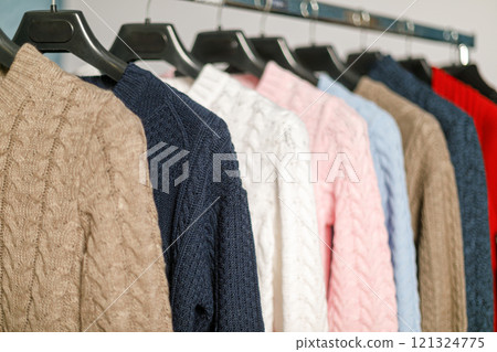 Row of knitted sweaters in soft colors showcased on hanger rack 121324775