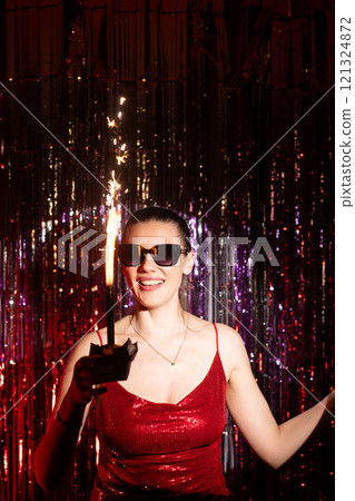 A stylish woman wearing a stunning red dress enjoys a vibrant festive atmosphere while celebrating with a sparkler A stylish woman wearing a stunning red dress enjoys a vibrant festive atmosphere while celebrating with a sparkler 121324872