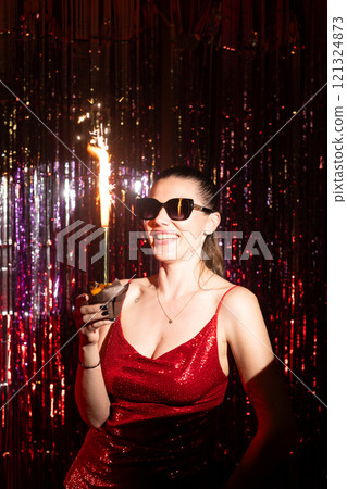 A stylish woman wearing a stunning red dress enjoys a vibrant festive atmosphere while celebrating with a sparkler A stylish woman wearing a stunning red dress enjoys a vibrant festive atmosphere while celebrating with a sparkler 121324873