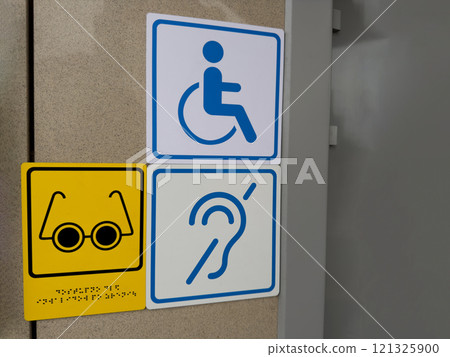 Signs on wall at entrance to building for disabled people, wheelchair sign, icon of deaf person and person with limited vision with braille text, modern accessible area for people with health problem 121325900