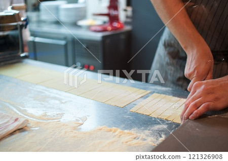 A chef prepares pasta by cutting and rolling the raw dough on a metal countertop. 121326908