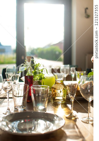 A table with drinks, glasses and goblets standing on a wooden table in a restaurant lit by the afternoon sun 121327355