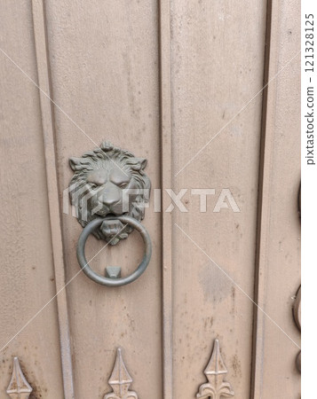 An antique lion head door knocker crafted in metal, set against a rustic wooden panel. The piece combines functionality with decorative sophistication 121328125