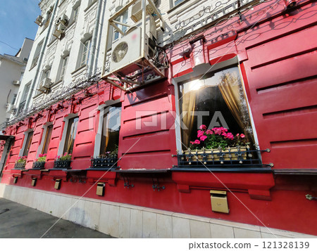 A vibrant red building exterior with decorative black wrought-iron details and blooming potted plants. The ornate canopy and bright flowers add charm and contrast to the bold architecture. 121328139