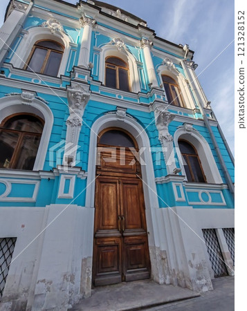The facade of a classical-style building painted in vivid blue, featuring tall windows, statues, and a grand entrance. It evokes the elegance of past architectural traditions. 121328152