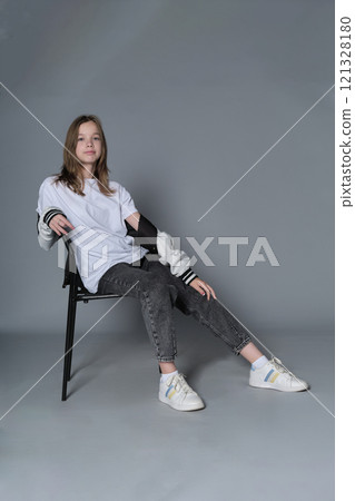 A teenage girl sits casually in a chair, her gaze steady and assured. Her posture reflects the self-confidence and ease of todays youth, embracing a minimalist style. A teenage girl sits casually in a chair, her gaze steady and assured. Her posture reflects the self-confidence and ease of todays youth, embracing a minimalist style. 121328180