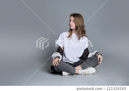 A girl in a casual outfit sits cross-legged, lost in thought. This image highlights the blend of innocence and emerging maturity, symbolizing the journey of self-discovery and individuality. A girl in a casual outfit sits cross-legged, lost in thought. This image highlights the blend of innocence and emerging maturity, symbolizing the journey of self-discovery and individuality. 121328183