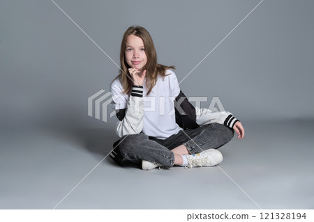A teenage girl sits casually with her legs crossed, her expression contemplative. Her pose symbolizes the reflective and self-aware aspects of adolescence in a modern context. 121328194