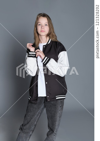 A teenage girl in profile with a varsity jacket resting on her shoulder, giving off a relaxed vibe. Her natural expression highlights youthful energy and individuality. 121328202