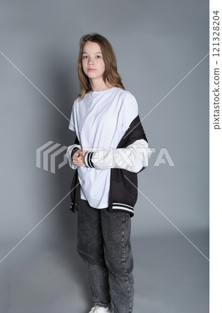 Side view of a teenage girl casually draping a varsity jacket over her shoulder. Her soft smile and laid-back posture capture a sense of youthful confidence and comfort. 121328204