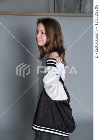 A young girl looks over her shoulder with a gentle expression, her jacket loosely draped around her. This image captures the quiet confidence and introspective nature of youth. A young girl looks over her shoulder with a gentle expression, her jacket loosely draped around her. This image captures the quiet confidence and introspective nature of youth. 121328208