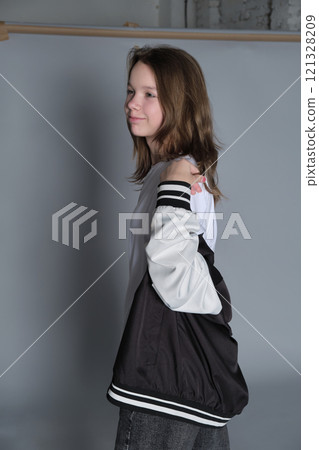 The young girl poses with her jacket loosely over her shoulders, embodying relaxed confidence. This image reflects the simplicity and authenticity often seen in contemporary youth culture. 121328209