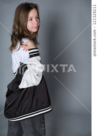 A girl turns slightly, looking thoughtfully to the side, her jacket resting on her shoulder. This portrait expresses the blend of innocence and emerging maturity seen in adolescence. A girl turns slightly, looking thoughtfully to the side, her jacket resting on her shoulder. This portrait expresses the blend of innocence and emerging maturity seen in adolescence. 121328211