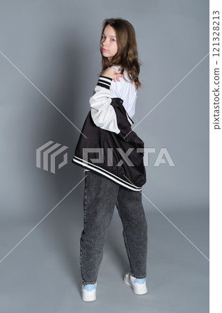 The young girl stands in profile, gazing softly with her jacket casually draped. This image highlights the beauty of a natural, unguarded moment, often found in todays lifestyle portraits. The young girl stands in profile, gazing softly with her jacket casually draped. This image highlights the beauty of a natural, unguarded moment, often found in todays lifestyle portraits. 121328213