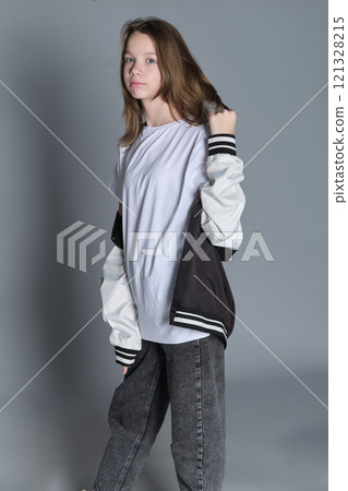 A teenage girl in a relaxed, modern outfit holds her jacket, conveying a sense of style and freedom. This image reflects the trend of embracing casual fashion as a form of personal expression. A teenage girl in a relaxed, modern outfit holds her jacket, conveying a sense of style and freedom. This image reflects the trend of embracing casual fashion as a form of personal expression. 121328215