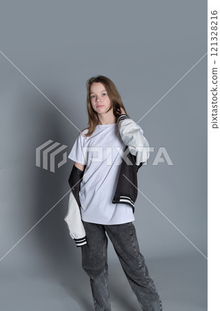 A young girl stands confidently in casual attire, one hand resting on her jacket. This image showcases the modern approach to youth fashion, blending comfort with a sense of style. A young girl stands confidently in casual attire, one hand resting on her jacket. This image showcases the modern approach to youth fashion, blending comfort with a sense of style. 121328216