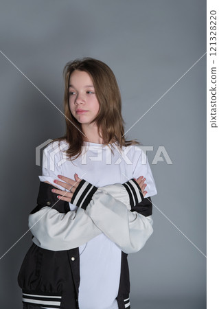 A teenage girl strikes a casual pose, wearing jeans and a varsity jacket over a white shirt. Her outfit represents youthful confidence and the freedom of self-expression in everyday wear. 121328220