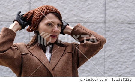 A stylish woman wearing gloves fixes her warm hat, blending fashion with practicality. A stylish woman wearing gloves fixes her warm hat, blending fashion with practicality. 121328226
