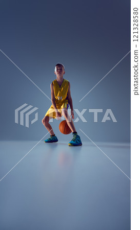 Sportive teenage boy, playing basketball using different techniques to confuse opponent and win match against grey studio background. 121328580