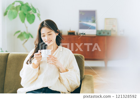 A woman sitting on a sofa and drinking coffee A woman sitting on a sofa and drinking coffee 121328592