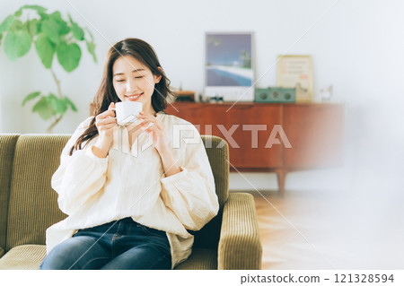 一個女人坐在沙發上，喝著咖啡 121328594