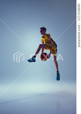 Competitive teenager, basketball athlete jumping in mid air with ball to get powerful slam dunk against grey studio background. 121328600