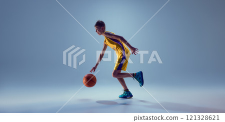 Side view photo of junior basketball player training dribbling technique in motion against grey studio background. Side view photo of junior basketball player training dribbling technique in motion against grey studio background. 121328621