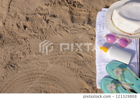 Beach essentials: towel, hat, sunglasses, sunscreen, and sandals on sandy beach Beach essentials: towel, hat, sunglasses, sunscreen, and sandals on sandy beach 121329808