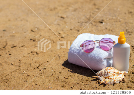 Beach essentials: sunglasses, towel, sunscreen, and seashell on sandy shore 121329809