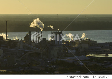Huge factory with high chimneys polluting atmosphere with carbon dioxide smoke from production process at plant manufacturing yard. Industrial site at sunset 121330172