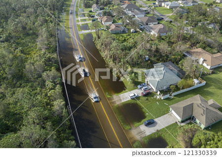 Flooded american street with moving vehicles and surrounded with water houses in Florida residential area. Consequences of hurricane natural disaster Flooded american street with moving vehicles and surrounded with water houses in Florida residential area. Consequences of hurricane natural disaster 121330339