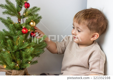 A small child looks at the New Year's decorations on a green New Year's tree 121332108