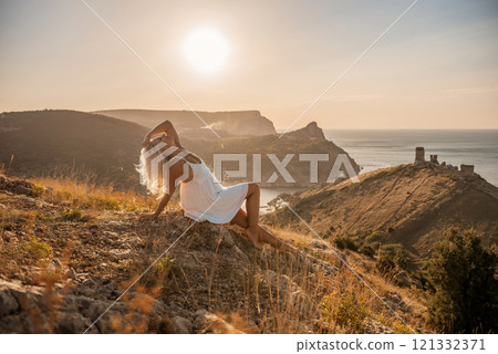 A woman is sitting on a hillside overlooking the ocean. She is wearing a white dress and has blonde hair. The scene is serene and peaceful, with the ocean in the background. A woman is sitting on a hillside overlooking the ocean. She is wearing a white dress and has blonde hair. The scene is serene and peaceful, with the ocean in the background. 121332371