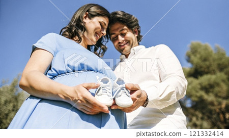 Pregnant woman and man holding small baby shoes 121332414