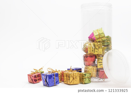 Colorful miniature gift boxes lie in a clear plastic jar and on its side against a white background. 121333925