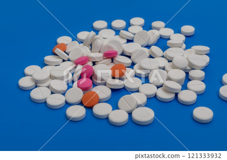 Assorted pills and tablets scattered on a vibrant blue surface 121333932