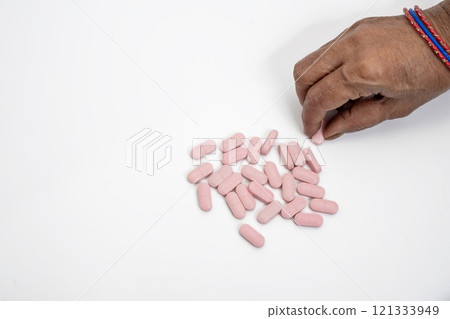 Female hand taking a pink pill on a white background, top view Female hand taking a pink pill on a white background, top view 121333949