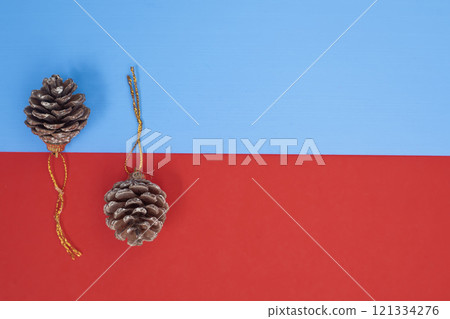 Brown pine cones with golden string loops on a vibrant blue and red background 121334276