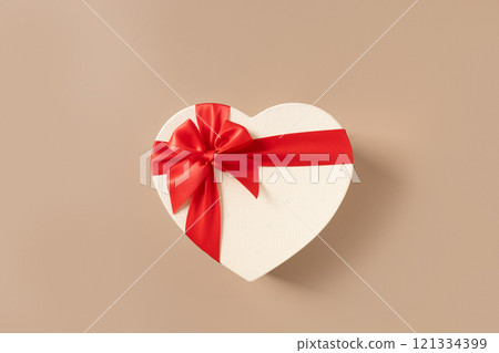 Valentines day white gift with red bow in shaped of heart on beige background. Top view. Greeting card. Valentines day white gift with red bow in shaped of heart on beige background. Top view. Greeting card. 121334399