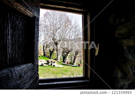 Interior view from the window of a rustic house towards a beautiful garden with trees 121334993