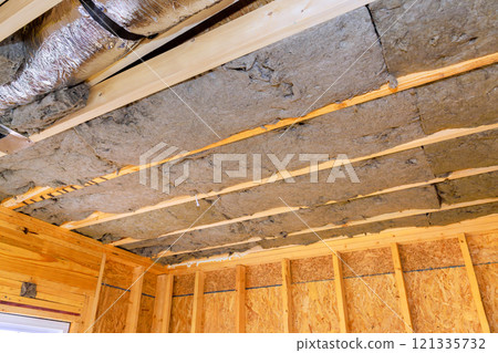 Installing insulation between exposed beams in wooden structure for improved energy efficiency during construction new house 121335732