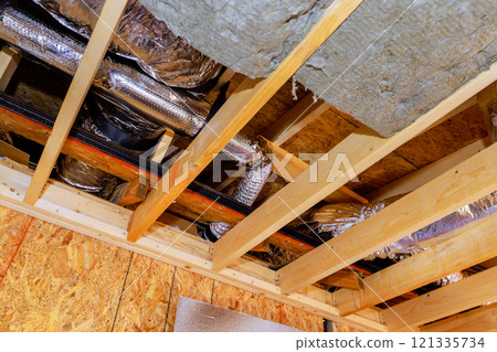 Installing insulation, ductwork with in ceiling framework of at new home, construction site. 121335734