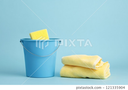 Cleaning supplies bucket and sponge with folded towels on blue background 121335904